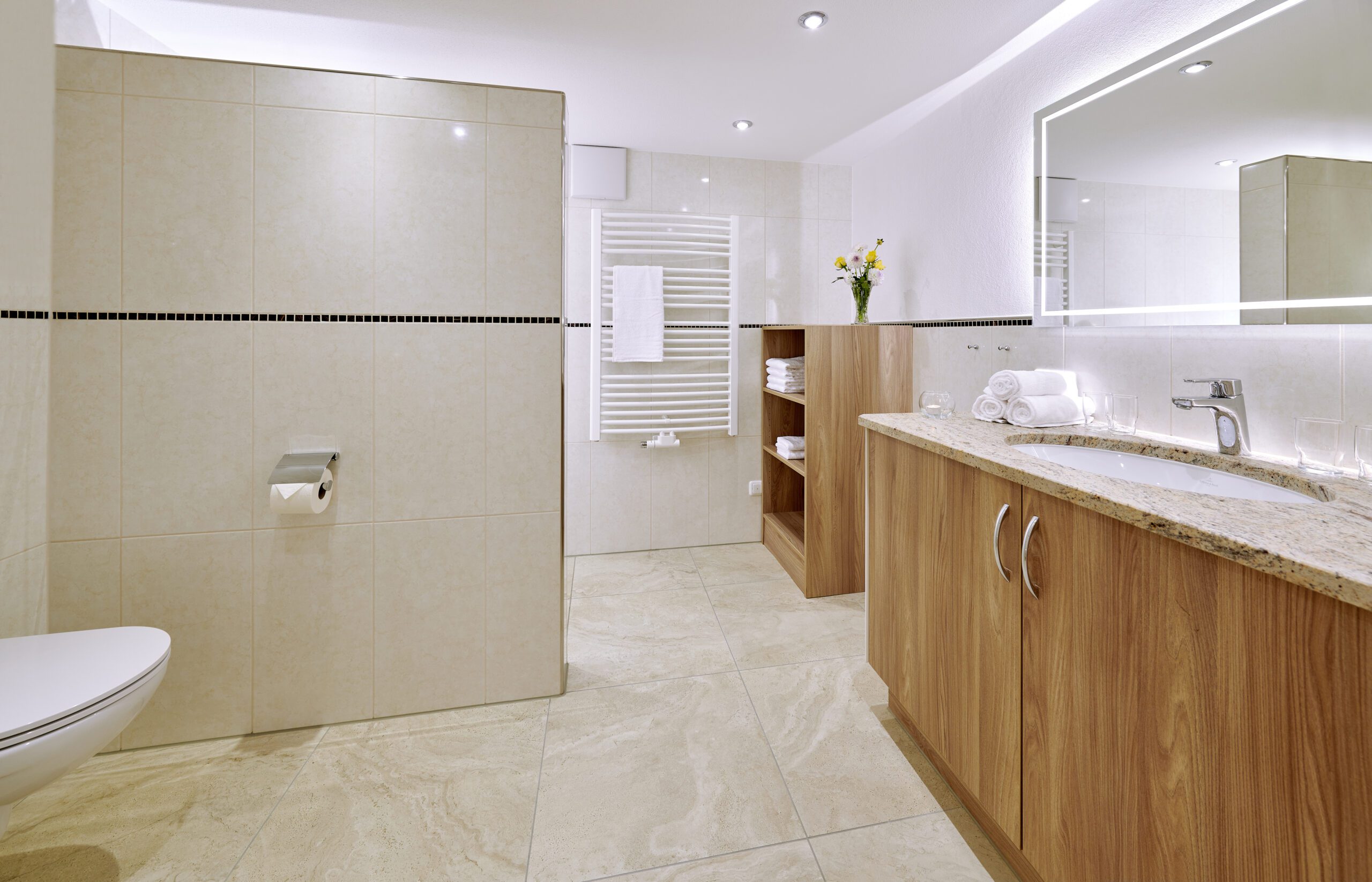 modernes badezimmer mit begehbarer dusche, bodenfliesen sind beige und die wandfliesen sind glaenzend-weiss, der waschtisch ist aus beige-melierten granit